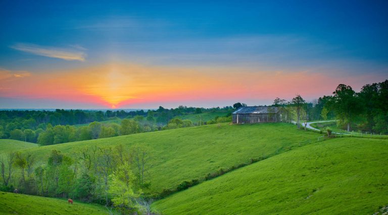 Sunset over rolling green hills and a barn in the Kentucky countryside